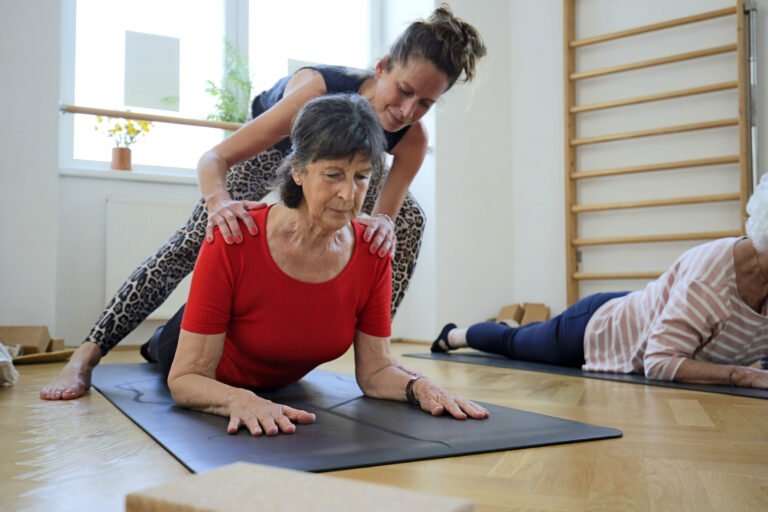 Yogalehrerin korrigiert die Yoga-Pose einer Seniorin